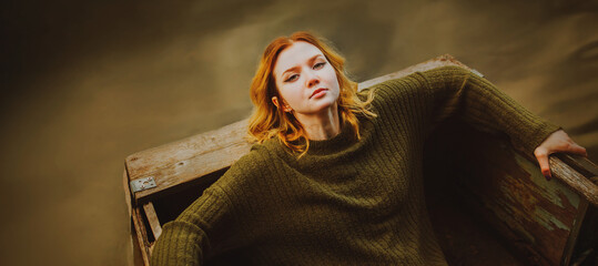 A beautiful blonde woman in a vintage green sweater lies in an old wooden boat floating on the...