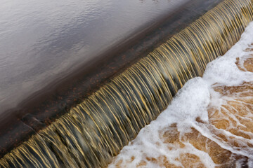 Iron containing water flows foaming over a dam, constructed for water level management
