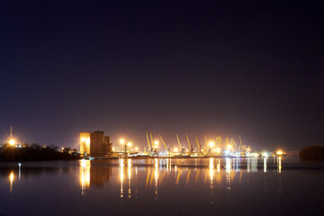 Night scene of river port cranes with reflections on the water. Cargo Port at Night