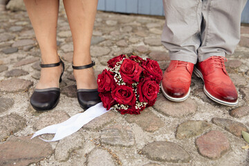 Braut und Bräutigam stehen nebeneinander mit einem Brautstrauß aus roten Rosen - 559852662