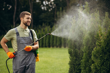 Garden worker watering grass and bushes in the yard with sprinkler