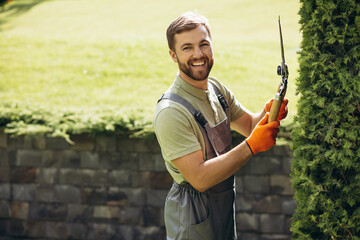 Garden worker trimming bushes with scissors in the yard