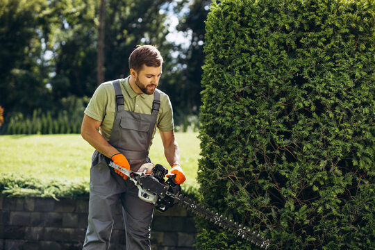 Man worker cutting bushes with an electric saw in the yard