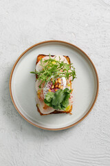 Toast with grilled shrimps and vegetables, poached egg and herbs on top served in restaurant.