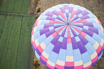 arial view of large pink, purple, and blue hot air balloon from the top rising over a bright green field