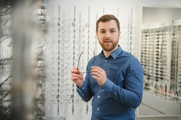 In Optics Shop. Portrait of male client holding and wearing different spectacles, choosing and...