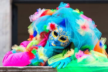 persona ritratta con costume di carnevale a venezia. maschera multi colore, con mano destra la mento