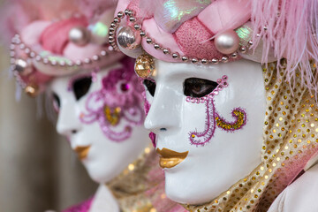 coppia di maschere al carnevale di venezia, primo piano sui volti di profilo, tonalità rosa