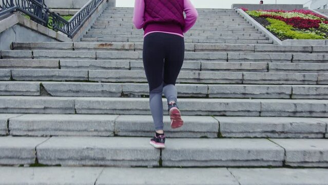 Fit girl in sportswear runs up urban stairs. Faceless sportswoman doing cardio workout on staircase outside. Blonde woman is in hurry, quickly overcoming distance along street stairway
