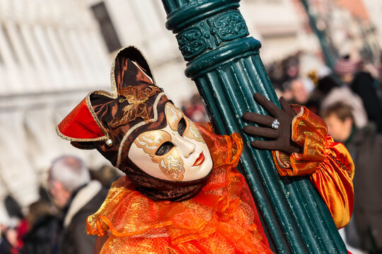 maschera di carnevale di venezia, abbracciata ad un palo verde con in mostra la mano guantata dove si vede un anello.