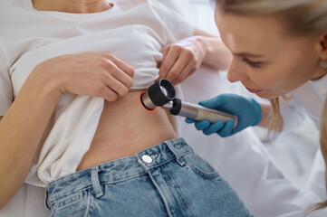 Dermatologist examining patient with magnifying glass in clinic