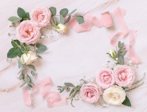 Pink and cream roses and silk ribbons on white marble top view, Romantic wedding background