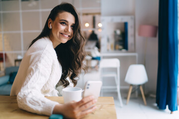 Smiling woman with coffee and cellphone at home