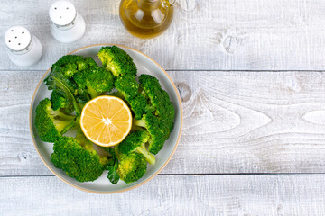 Boiled broccoli with lemon and olive oil in a plate. Wooden background.  Healthy food. Top view....
