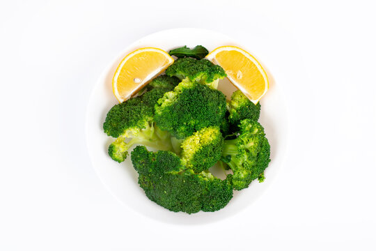 Boiled broccoli with lemon in a plate. Isolated on white background. Top view