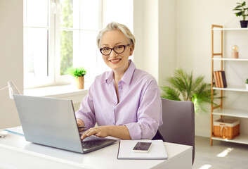 Middle age woman sitting at desk working with laptop computer. Attractive successful gray haired...
