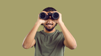 Young happy unshaven man looks at you with smile through binoculars symbolizing search for hobby or...