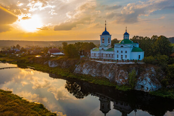 Fototapeta premium sunset with the rays of the sun on the background of the domes of the temple on the rock by the river, a beautiful view of the village in Russia