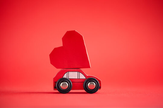 Red model of car delivering red paper heart on red background. Creative greeting card for Saint Valentine day.