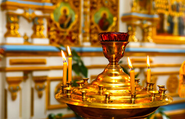 A candlestick with lighted candles in front of icons in an Orthodox church. The concept of...