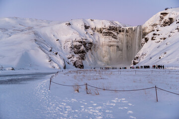 imagen de  la cascada de Skógafoss con el entorno nevado, y una capa de hielo cubriendo el río....