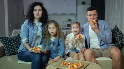 Parents and kids with zombified expression watch movie on TV. Adults and sister siblings addicted to watch TV and eating pizza in apartment