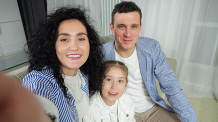 Fototapeta premium Parents and daughter enjoy talking with relatives on videocall. Junior schoolgirl with amused expression talks about life issues and family waves goodbye