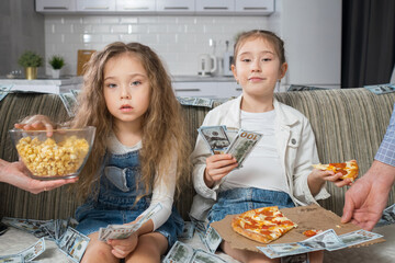 Girl kids enjoy sitting among money banknotes on sofa and receive food from parents-servants....