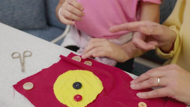 Unrecognizable senior woman teaching a young girl how to sew buttons 