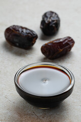 Date syrup in a small glass bowl nearly whole date fruits. Close up. Beige background with stone texture. Eco natural sweetener. Sweet healthy sauce to add to drinks, porridge and pancakes
