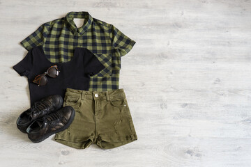 Stylish women's or teenager's clothing set with accessories: checkered shirt, black jersey top, green jeans shorts, sunglasses and boots in military style. Summer female outfit