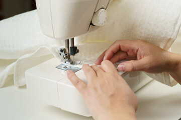 A female seamstress sews white fabric items on a sewing machine.