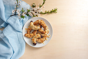 Almond crescent cookies on a plate, spring flower branch and blue napkin on a light wooden table,...