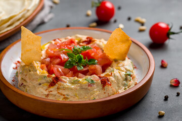Traditional homemade hummus with fresh tomatoes and red onion on grey table macro close up