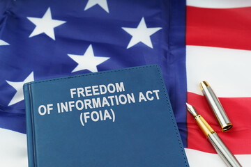 On the US flag lies a pen and a book with the inscription - FREEDOM OF INFORMATION ACT - FOIA