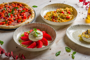 Salad with buratta cheese and tomatoes on bowl, pizza with roastbeef and tomatoes, fried camambert with truffle and pasta tagliatelli with shrimps on marble table