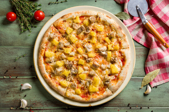 pizza Hawaiian with pineapple and chicken top view on green wooden table