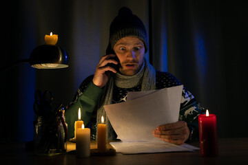 shocked man in candle light looking at high bills for electricity, gas heating in cold dark room at...