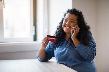 Woman looking at credit card, confirm purchase via telephone call