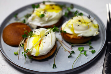 Poached eggs with microgreens on a crispy bun on a plate.