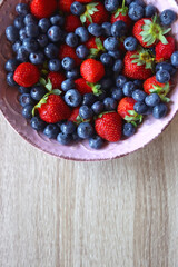 Pink rustic bowl filled with fresh blueberries and strawberries. Wooden background, top view.