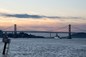 ship traveling under bay bridge at sunset with Golden Gate in background