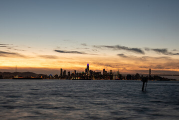 sunset behind San Francisco skyline across bay with buildings lit and bridge