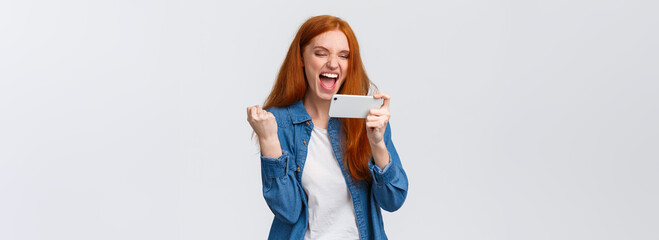 Confident and sassy good-looking redhead woman beat score, watching tennis match online on smartphone and cheering for player, fist pump delighted, celebrating success, winning in mobile game