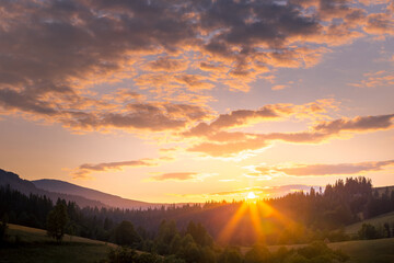 Stunning sunset sky with clouds over green forest hills. Summer countryside view. Carpathian mountains. Ukraine.