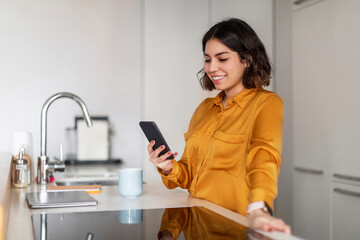 Fototapeta na wymiar Happy Young Arab Woman Making Online Shopping With Smartphone In Kitchen