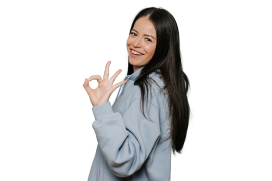 Long haired young brunette caucasian woman dressed in pastel lilac hoodie shows ok gesture, broad smiling over transparent background with satisfied expression. Promo and sales template.