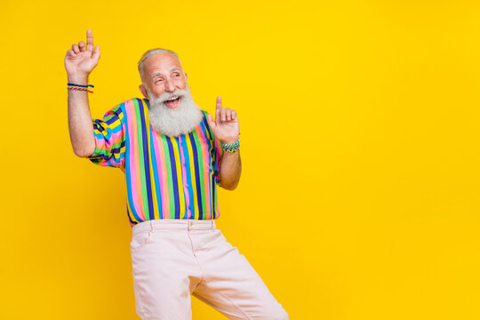 Photo of funky good mood man wear colorful shirt rising having fun pointing fingers up empty space isolated yellow color background