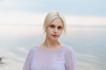 Blonde girl on a summer day on the shore near the river in nature in a dress