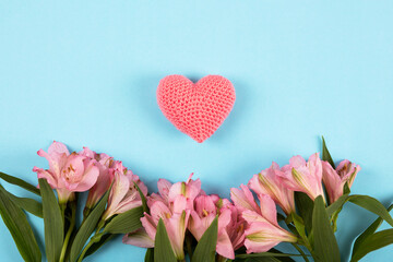 Soft purple flowers Alstroemeria with a knitted pink heart on a blue background for Valentine's Day greetings, gift card